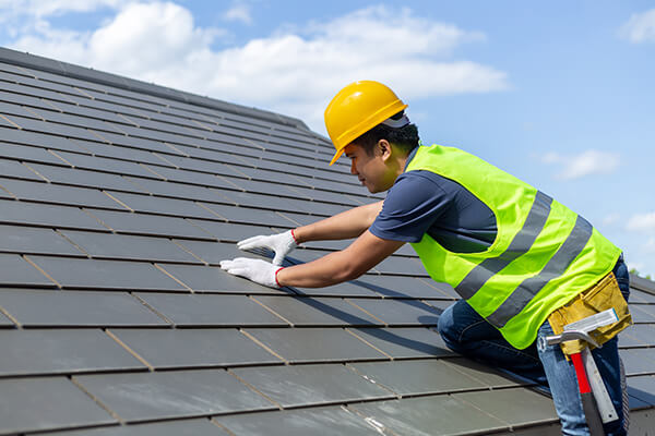 worker with white gloves replacing gray tiles or shingles on a house
