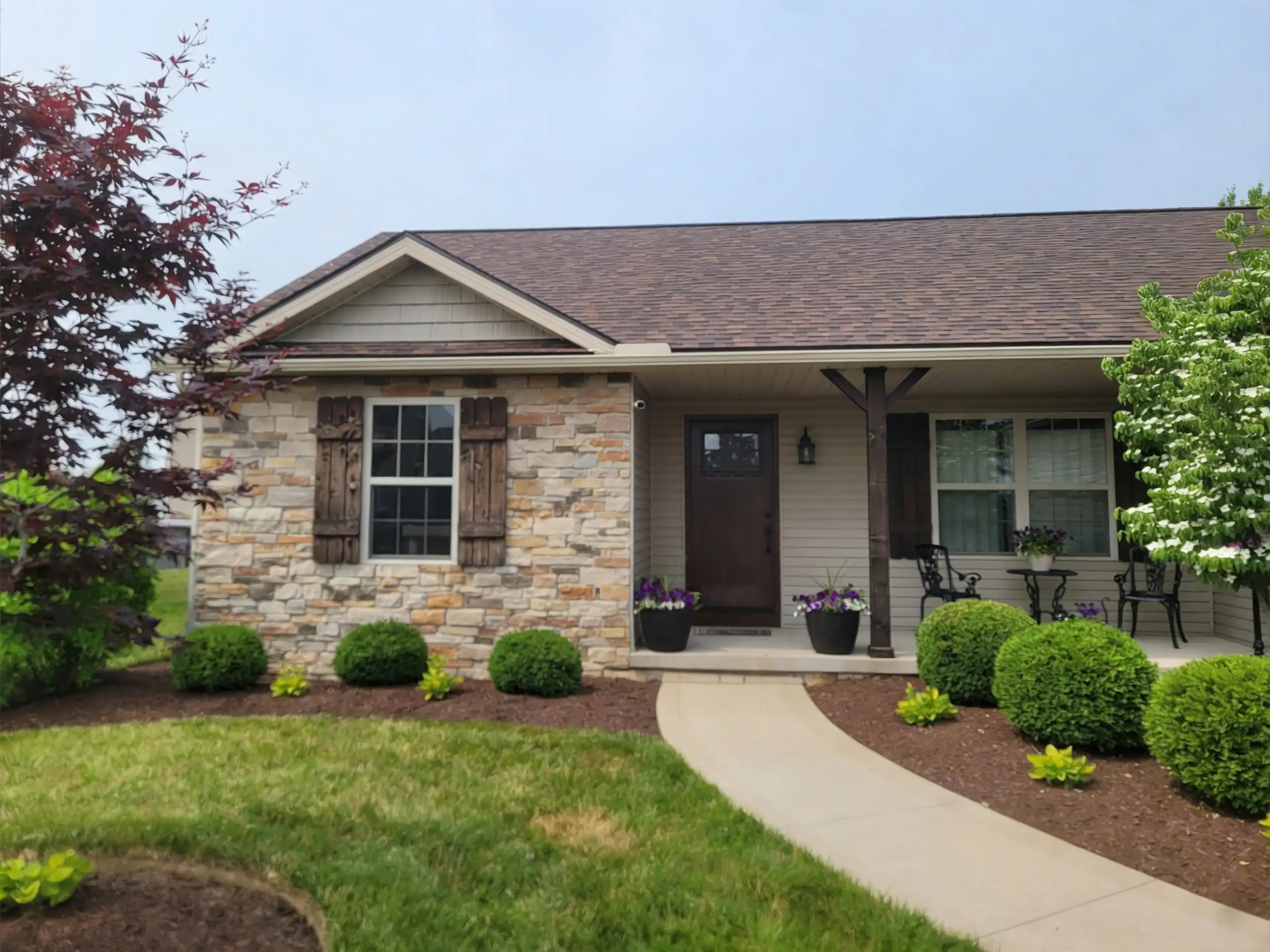 Residential front with brown asphalt shingle roof, stone veneer facade, covered porch and manicured landscaping