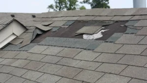 Roof replacement: damaged asphalt shingles with lifted and missing pieces exposing roof underlayment