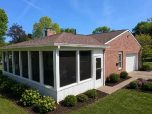 Brick house with white-framed screened porch (sunroom), asphalt shingle roof, gutters and landscaped shrubs for home improvement loans